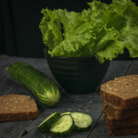 Fresh cucumbers with lettuce leaves and bread on a black wooden table. Healthy eating.