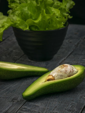 Cut avocado fruit on a black wooden table. Plant-based food.