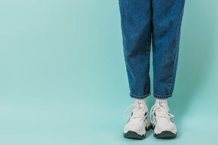 Legs of a girl in white socks, white sneakers and jeans on a blue background. Stylish youth clothing and shoes. Place for text.の写真素材