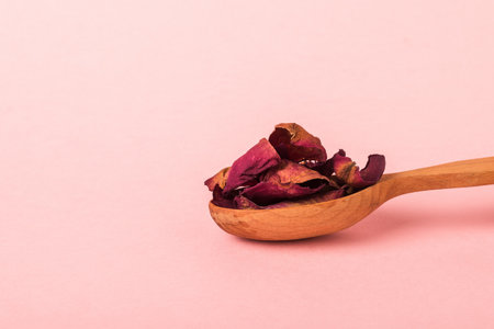 Dry rose petals in a wooden spoon on a pink background. The herbarium of roses.の写真素材