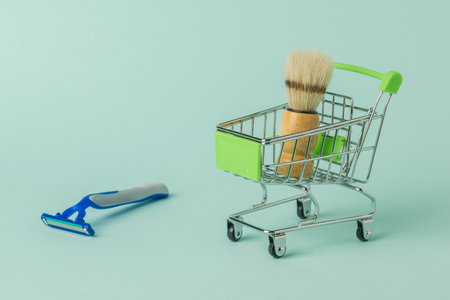 A shaving brush in a shopping cart and a disposable razor on a blue background. Set for care of a man's face.の写真素材