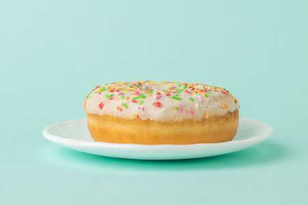 Fresh decorated donut on a white plate on a blue background. A popular confection.の写真素材