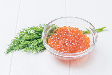 A glass bowl with red caviar on a white wooden table. Natural healthy marine product.の写真素材