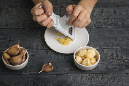 A girl grates garlic on a grater on a wooden table. A popular spice for the kitchen.の写真素材