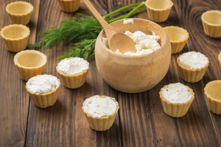Wooden bowl with cream cheese and tartlets on a wooden table. The process of preparing a delicious snack.の写真素材