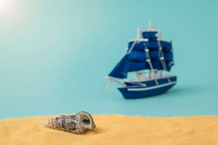 A seashell on the sand against a sailboat on a blue background. The concept of travel and adventure.の写真素材