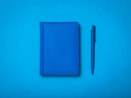 Blue ballpoint pen and blue notepad on a blue background. Monochrome image of office accessories.の写真素材