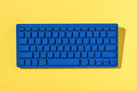 Bright blue keyboard in bright hard light on yellow background. Monochrome image of office accessories.の写真素材