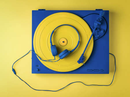Vintage vinyl record player and blue headphones on a yellow background. Retro music equipment.