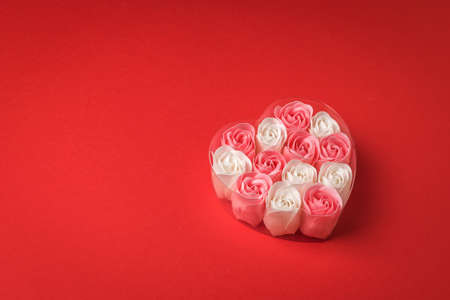 Red and white rose buds in a heart-shaped box on a red background. The concept of love.の写真素材