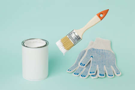 Floating brush with white paint on the background of gloves and paint cans. Execution of painting...