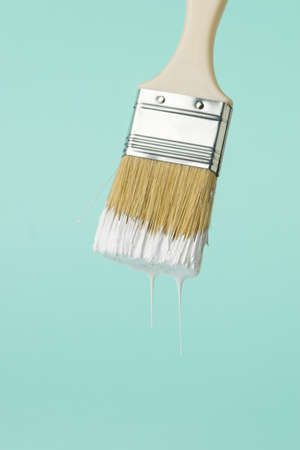 Brush with dripping white paint on a blue background. Execution of painting works.の写真素材