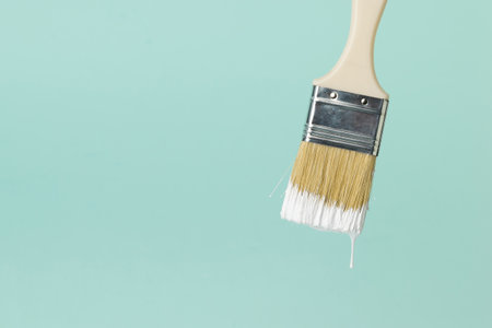 Brush with dripping white paint on a blue background. Execution of painting works.の写真素材