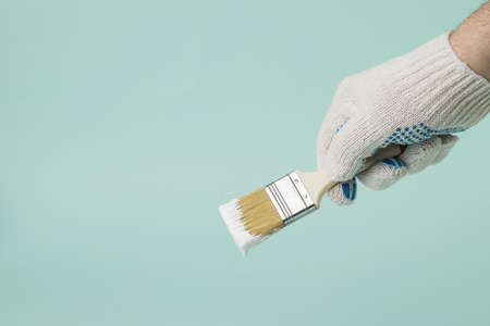 A man wearing gloves holds a brush with dripping white paint on a blue background. Execution of painting works.の写真素材
