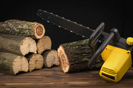 Electric chain saw saws wooden logs on a wooden background. Electric tool for wood processing.の写真素材