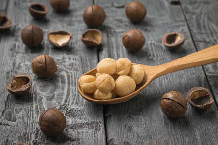 Wooden spoon with peeled macadamia nuts and unpeeled on a wooden table. Superfood.
