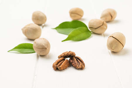 Three peeled pecans and unpeeled nuts on a white wooden table. Vegetarian food.の写真素材