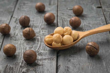 A wooden spoon with peeled macadamia nuts and scattered unpeeled nuts. Superfood.の写真素材