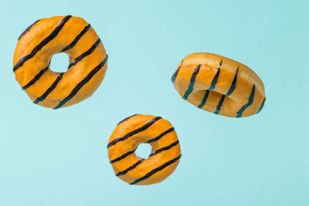 Three glazed orange donuts flying on a blue background. Popular sweet pastries.の写真素材