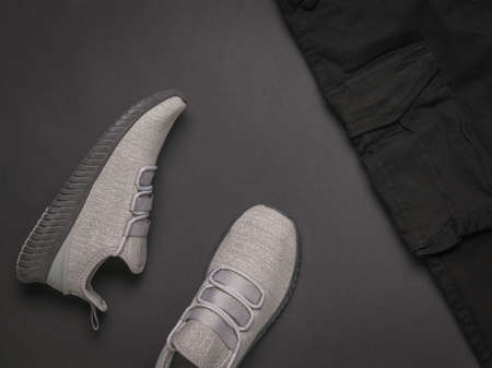Gray sneakers and black pants with a large pocket on a dark gray background. Fashionable youth casual clothing.の写真素材