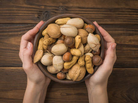 Women's hands hold a clay bowl with a mixture of nuts. Vegetarian food.の写真素材