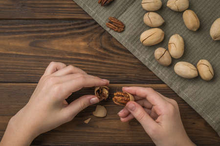 Women's hands peel pecans from their shells on a wooden table. Vegetarian food.の写真素材