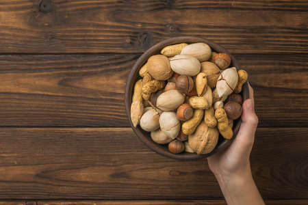 A woman's hand holds a bowl filled with nut mixture on a wooden background. Vegetarian food.の写真素材