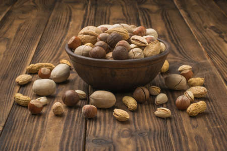 The nut mixture is poured out of an earthenware bowl on a dark wooden table. Vegetarian food.の写真素材