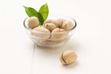 A glass bowl of pecans on a white wooden table. Vegetarian food.
