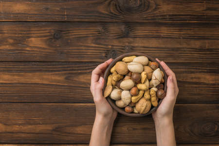 Women's hands with a bowl filled with nut mixture on a wooden rustic table. Vegetarian food.の写真素材