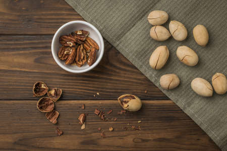 Pecans on a coarse cloth and a bowl of peeled nuts on a wooden table. Vegetarian food.