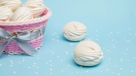 Wicker basket with fresh meringue and jam on a blue background. Delicious sweetness of eggs and...