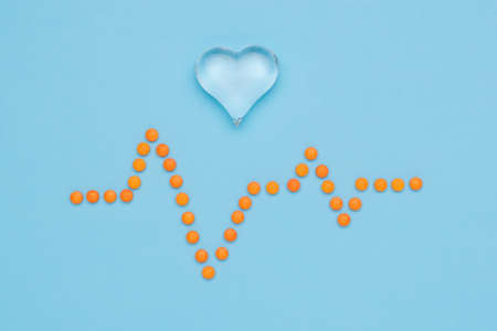 A drawing of a cardiogram made of orange pills and a glass heart on a blue background. The concept...