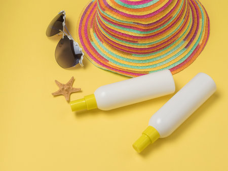 Two tubes of sunscreen, a hat and glasses on a yellow background. Taking a sun bath. Sun therapy.の写真素材