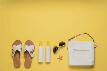 Women's bag, sandals and suntan products on a yellow background. Vacation concept. Flat lay.の写真素材