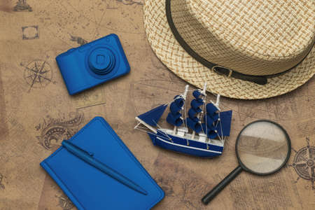 A hat, a model ship, a camera, and a notebook on the background of an old map. The concept of travel...