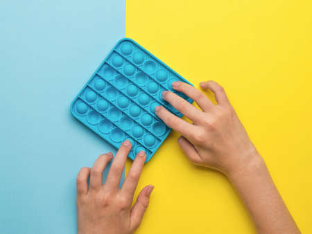 A girl plays a popular pop it toy on a yellow and blue background. A popular anti-stress product.の写真素材