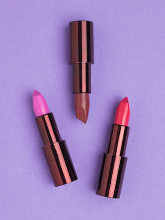 Three colors of fashionable lipstick on a purple background. Lip decoration.