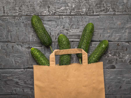 A paper bag with spilled cucumbers on a wooden table. Fresh vegetables in eco-friendly packaging.の写真素材