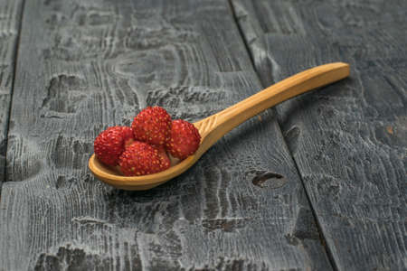 Wooden spoon with wild strawberries on a wooden table. Fresh crop.