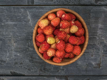 Top view of a wooden bowl with wild strawberries on a wooden table. Fresh crop.の写真素材