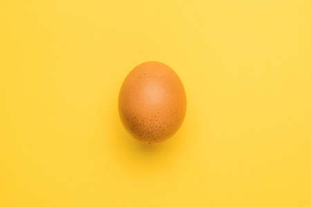 A whole brown chicken egg on a yellow background. A natural product.