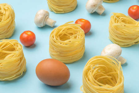 Pasta, egg, tomatoes and mushrooms on a blue background. Ingredients for making pasta.の写真素材