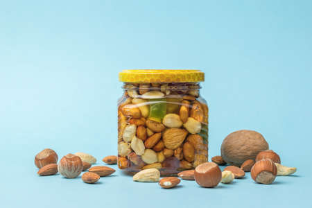 A glass jar with honey and nuts and scattered nuts on a blue background. A natural nourishing remedy.の写真素材