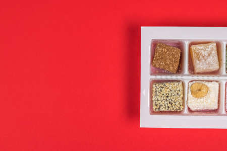 Pieces of Turkish delight in a plastic container on a red background. Oriental sweets. Flat lay.の写真素材