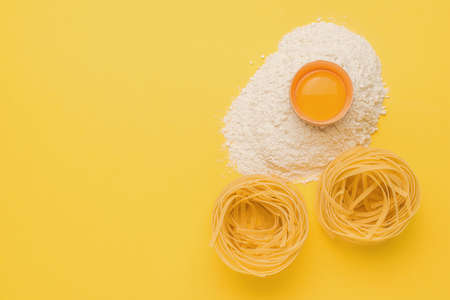 A broken egg, flour and two pieces of pasta on a yellow background. Natural products and kitchen equipment.の写真素材