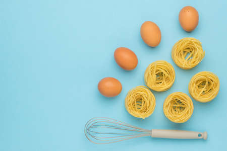 Eggs, pasta and a whisk for whipping on a blue background. Ingredients for making pasta.の写真素材