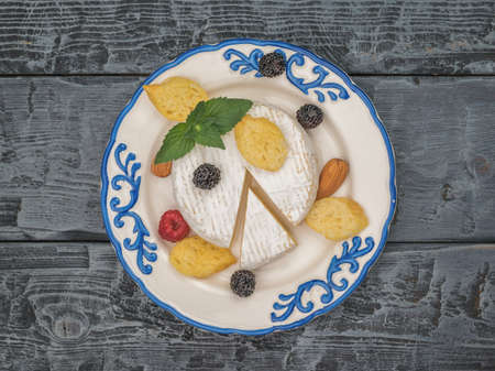 Top view of a plate with camembert cheese and berries on a wooden table. A product made from natural...