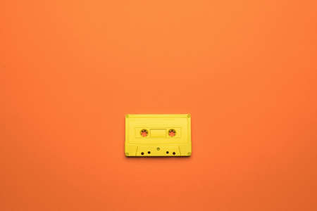 A bright yellow cassette with a magnetic tape on an orange background. Stylish retro equipment for...