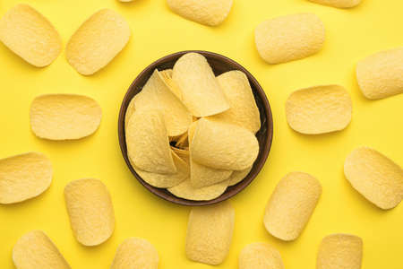 Potato chips and a clay bowl on a yellow background. A popular potato dish. Flat lay.